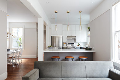 Photo of a transitional l-shaped open plan kitchen in San Francisco with shaker cabinets, white cabinets, quartz benchtops, white splashback, subway tile splashback, stainless steel appliances, medium hardwood floors, a peninsula and brown floor.