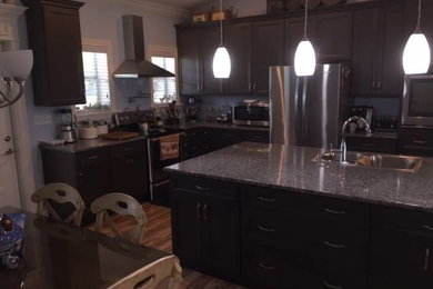 Example of a mid-sized transitional l-shaped medium tone wood floor eat-in kitchen design in New Orleans with a double-bowl sink, recessed-panel cabinets, dark wood cabinets, multicolored backsplash, stainless steel appliances and an island