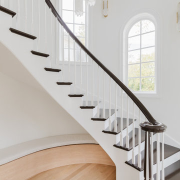 Two-Story Curved Staircase Framed by Arched Windows and Light Oak Flooring