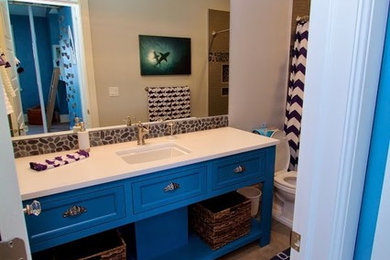 Mid-sized beach style bathroom in Salt Lake City with an undermount sink, recessed-panel cabinets, blue cabinets, engineered quartz benchtops, an alcove tub, a shower/bathtub combo, a one-piece toilet, gray tile, grey walls and light hardwood floors.