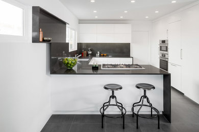 Photo of a contemporary u-shaped eat-in kitchen in Los Angeles with flat-panel cabinets, white cabinets, panelled appliances, a peninsula, quartz benchtops, black splashback and an undermount sink.