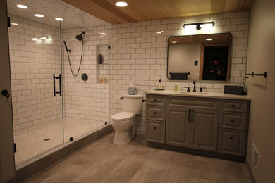 Large transitional white tile and ceramic tile porcelain tile alcove shower photo in Detroit with raised-panel cabinets, gray cabinets, a two-piece toilet, gray walls, an undermount sink and quartz countertops