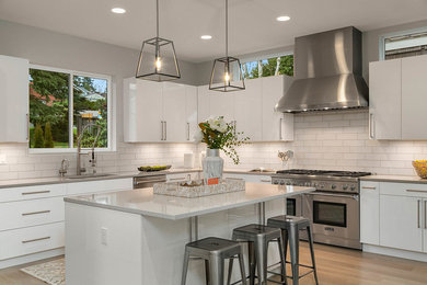 Inspiration for a contemporary l-shaped kitchen in Seattle with an undermount sink, flat-panel cabinets, white cabinets, white splashback, subway tile splashback, stainless steel appliances, light hardwood floors, with island, beige floor and grey benchtop.