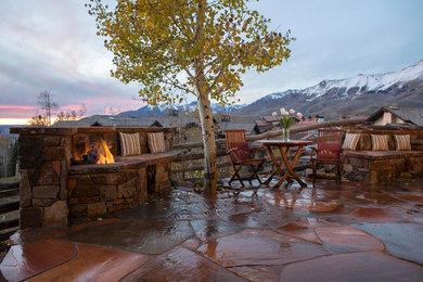 Large country backyard patio in Denver with natural stone pavers, a fire feature and no cover.