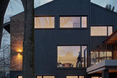 Large modern brown three-story wood and board and batten house exterior idea in Montreal with a shingle roof and a brown roof