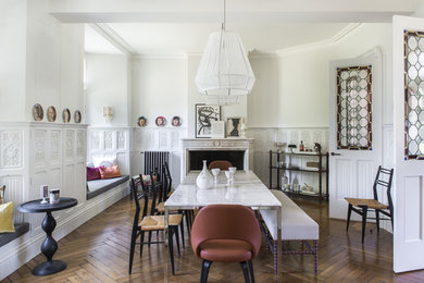 This is an example of an expansive eclectic separate dining room in Paris with white walls, medium hardwood floors, a standard fireplace and a stone fireplace surround.