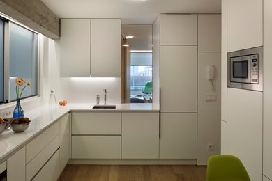 Enclosed kitchen - mid-sized modern l-shaped medium tone wood floor enclosed kitchen idea in Other with an undermount sink, flat-panel cabinets, white cabinets, solid surface countertops, white backsplash, stainless steel appliances, no island and white countertops