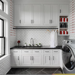 ニューヨークの大きいカントリー風おしゃれな家事室 (シェーカースタイル扉のキャビネット、白いキャビネット、白い壁、スレートの床、左右配置の洗濯機・乾燥機、黒い床、黒いキッチンカウンター、アンダーカウンターシンク) の写真