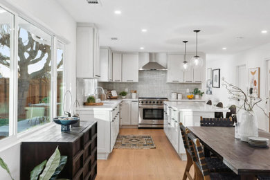Inspiration for a mid-sized transitional l-shaped eat-in kitchen in Sacramento with a drop-in sink, shaker cabinets, white cabinets, quartzite benchtops, grey splashback, mosaic tile splashback, stainless steel appliances, medium hardwood floors, with island and white benchtop.