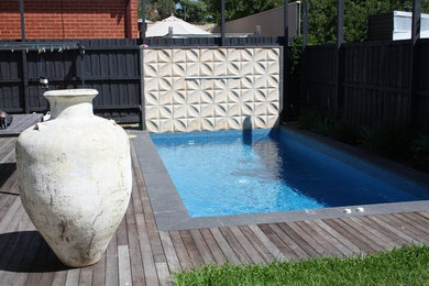 Modelo de piscina alargada actual de tamaño medio rectangular en patio trasero con granito descompuesto