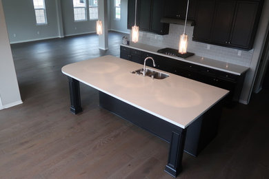 Example of a large minimalist medium tone wood floor and brown floor kitchen design in Los Angeles with a double-bowl sink, granite countertops, white backsplash, subway tile backsplash, stainless steel appliances and an island
