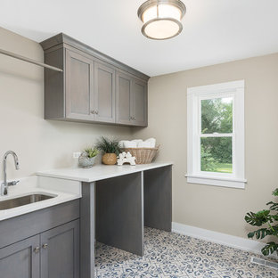 シカゴの中サイズのコンテンポラリースタイルのおしゃれな洗濯室 (アンダーカウンターシンク、シェーカースタイル扉のキャビネット、ヴィンテージ仕上げキャビネット、人工大理石カウンター、ベージュの壁、セラミックタイルの床、左右配置の洗濯機・乾燥機、マルチカラーの床、白いキッチンカウンター) の写真