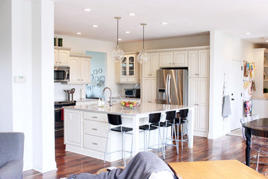 Example of a mid-sized classic l-shaped dark wood floor and brown floor eat-in kitchen design in Tampa with an undermount sink, white backsplash, stainless steel appliances, an island, raised-panel cabinets, white cabinets and granite countertops
