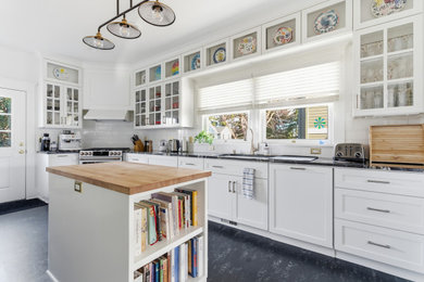 Kitchen - large craftsman black floor kitchen idea in Portland with an undermount sink, shaker cabinets, white cabinets, marble countertops, white backsplash, ceramic backsplash, white appliances, an island and black countertops