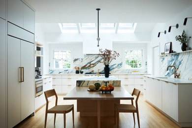 Inspiration for a large modern u-shaped light wood floor and vaulted ceiling kitchen remodel in New York with an undermount sink, flat-panel cabinets, light wood cabinets, marble countertops, marble backsplash, stainless steel appliances and an island