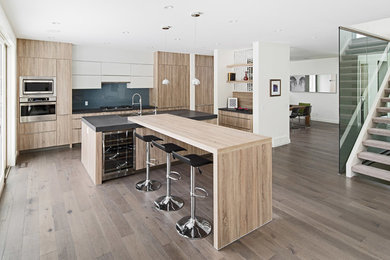 Design ideas for a large modern single-wall open plan kitchen in Calgary with a double-bowl sink, flat-panel cabinets, light wood cabinets, quartz benchtops, blue splashback, glass sheet splashback, panelled appliances, medium hardwood floors and multiple islands.