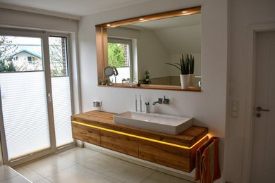Großes Modernes Badezimmer En Suite mit flächenbündigen Schrankfronten, hellbraunen Holzschränken, Eckbadewanne, bodengleicher Dusche, Wandtoilette mit Spülkasten, beigen Fliesen, Keramikfliesen, weißer Wandfarbe, Keramikboden, Aufsatzwaschbecken, Waschtisch aus Holz, beigem Boden, offener Dusche, brauner Waschtischplatte, Einzelwaschbecken, schwebendem Waschtisch, Tapetendecke und Tapetenwänden in Dortmund