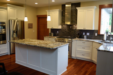 Eat-in kitchen - mid-sized traditional u-shaped medium tone wood floor and brown floor eat-in kitchen idea in Seattle with an undermount sink, shaker cabinets, white cabinets, granite countertops, gray backsplash, stainless steel appliances, an island and glass tile backsplash