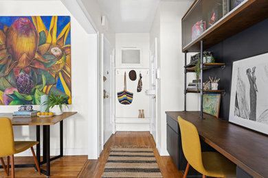 Inspiration for a small eclectic home office in New York with black walls, light hardwood floors and a built-in desk.