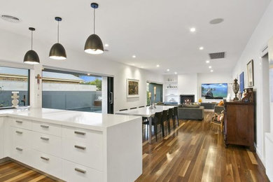 Inspiration for a large contemporary u-shaped open plan kitchen in Geelong with a drop-in sink, louvered cabinets, white cabinets, granite benchtops, brown splashback, glass sheet splashback, stainless steel appliances, dark hardwood floors, with island, brown floor and white benchtop.