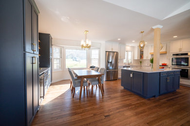Mid-sized transitional l-shaped medium tone wood floor and brown floor open concept kitchen photo in Omaha with shaker cabinets, blue cabinets, quartz countertops, white backsplash, ceramic backsplash, stainless steel appliances, an island and white countertops