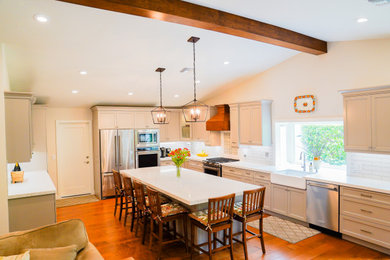 Inspiration for an expansive traditional u-shaped kitchen/diner in Orange County with a belfast sink, beaded cabinets, green cabinets, composite countertops, white splashback, ceramic splashback, stainless steel appliances, medium hardwood flooring, an island, orange floors, white worktops and exposed beams.
