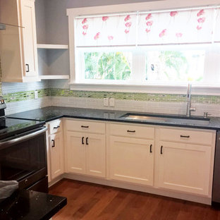 Photo of a mid-sized contemporary u-shaped kitchen pantry in Miami with white cabinets, green splashback, glass tile splashback, stainless steel appliances, medium hardwood floors and no island.