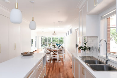 Mid-sized contemporary l-shaped eat-in kitchen in Sydney with a double-bowl sink, shaker cabinets, white cabinets, quartz benchtops, white splashback, subway tile splashback, stainless steel appliances, light hardwood floors, with island, beige floor and white benchtop.