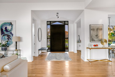 Photo of a large midcentury foyer in Dallas with white walls, light hardwood floors, a pivot front door, a black front door and brown floor.
