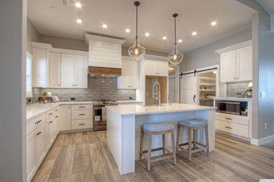 Example of a large cottage u-shaped laminate floor and gray floor kitchen pantry design in Seattle with a farmhouse sink, shaker cabinets, white cabinets, quartzite countertops, gray backsplash, ceramic backsplash, stainless steel appliances, an island and multicolored countertops