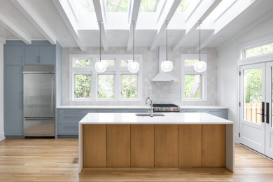 Example of a transitional single-wall light wood floor and exposed beam kitchen design in Raleigh with an undermount sink, flat-panel cabinets, quartz countertops, white backsplash, ceramic backsplash, stainless steel appliances, an island and white countertops