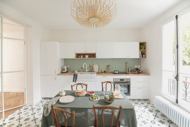 Aménagement d'une grande cuisine linéaire avec un évier 2 bacs, des portes de placard blanches, un plan de travail en bois, une crédence verte, carreaux de ciment au sol, aucun îlot et un sol multicolore.