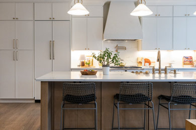 Example of a transitional galley dark wood floor and brown floor kitchen design in DC Metro with a farmhouse sink, recessed-panel cabinets, white cabinets, white backsplash, stone slab backsplash, paneled appliances, an island and white countertops
