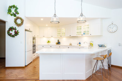 Photo of a large modern u-shaped separate kitchen in Gold Coast - Tweed with a double-bowl sink, glass-front cabinets, white cabinets, solid surface benchtops, white splashback, ceramic splashback, stainless steel appliances, medium hardwood floors and no island.