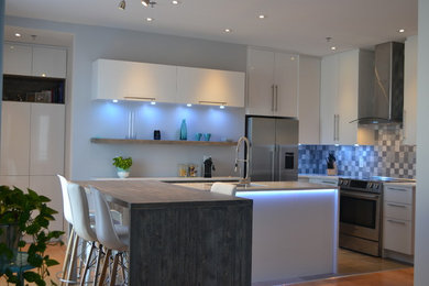 Mid-sized trendy l-shaped medium tone wood floor and brown floor open concept kitchen photo in Montreal with an undermount sink, flat-panel cabinets, white cabinets, wood countertops, gray backsplash, ceramic backsplash, stainless steel appliances and an island