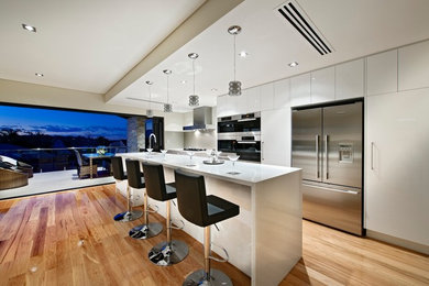 This is an example of a mid-sized modern u-shaped open plan kitchen in Perth with a double-bowl sink, flat-panel cabinets, white cabinets, solid surface benchtops, white splashback, ceramic splashback, stainless steel appliances, medium hardwood floors and with island.