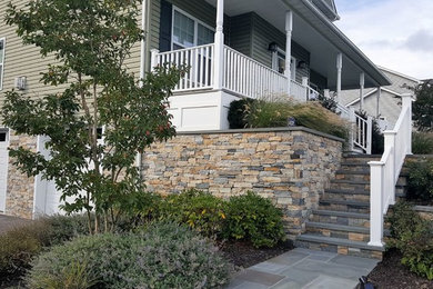 This is an example of a large traditional front yard verandah in New York with a roof extension and natural stone pavers.