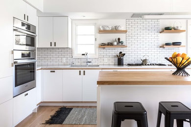Design ideas for a l-shaped kitchen in Sacramento with an undermount sink, flat-panel cabinets, white splashback, subway tile splashback, panelled appliances, light hardwood floors, with island and white benchtop.