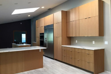 This is an example of a large contemporary l-shaped open plan kitchen in Miami with a farmhouse sink, flat-panel cabinets, stainless steel appliances, porcelain floors, with island, light wood cabinets and quartzite benchtops.