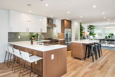 Trendy l-shaped light wood floor and beige floor kitchen photo in Other with a farmhouse sink, flat-panel cabinets, medium tone wood cabinets, green backsplash, glass tile backsplash, stainless steel appliances, an island and white countertops