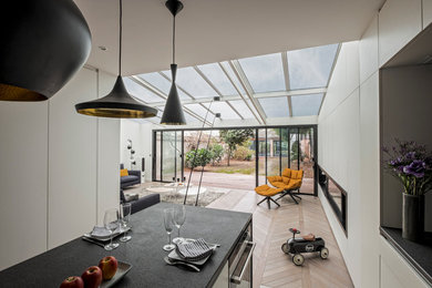 Cette image montre une cuisine ouverte linéaire design de taille moyenne avec un évier encastré, un placard à porte affleurante, des portes de placard blanches, un plan de travail en granite, une crédence noire, une crédence en dalle de pierre, un électroménager en acier inoxydable, parquet clair et îlot.