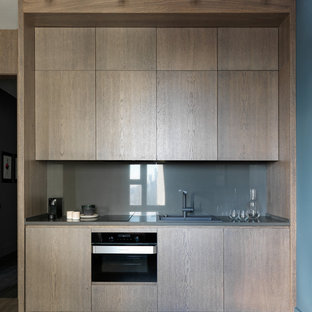 Неиссякаемый источник вдохновения для домашнего уюта: маленькая линейная кухня-гостиная в современном стиле с плоскими фасадами, фасадами цвета дерева среднего тона, столешницей из кварцевого композита, серым фартуком, черной техникой, паркетным полом среднего тона, коричневым полом, серой столешницей и накладной раковиной без острова