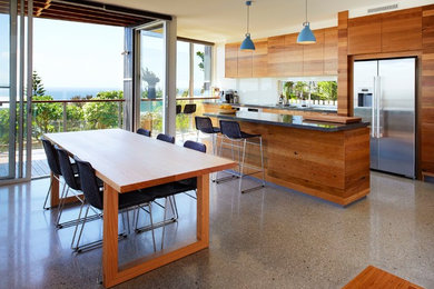 This is an example of a beach style kitchen in Sydney with medium wood cabinets, quartz benchtops, white splashback, concrete floors and with island.