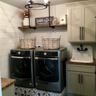 Modelo de cuarto de lavado de galera, campestre, de tamaño medio, con armarios estilo shaker, puertas de armario beige, encimera de madera, paredes grises, suelo de baldosas de cerámica, lavadora y secadora juntas, suelo negro y fregadero encastrado