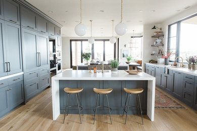 Inspiration for a large transitional u-shaped light wood floor and beige floor eat-in kitchen remodel in Los Angeles with an undermount sink, recessed-panel cabinets, blue cabinets, quartzite countertops, beige backsplash, stainless steel appliances, two islands and white countertops
