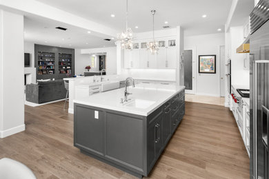Huge transitional u-shaped vinyl floor and brown floor open concept kitchen photo in Los Angeles with a farmhouse sink, recessed-panel cabinets, white cabinets, quartz countertops, white backsplash, quartz backsplash, stainless steel appliances, an island and white countertops