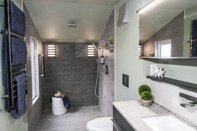 Photo of a mid-sized contemporary master bathroom in Philadelphia with furniture-like cabinets, brown cabinets, a curbless shower, a wall-mount toilet, gray tile, ceramic tile, green walls, ceramic floors, an undermount sink, granite benchtops, grey floor, an open shower and beige benchtops.