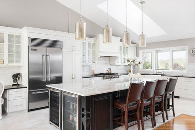 This is an example of a transitional l-shaped open plan kitchen in Calgary with recessed-panel cabinets, white cabinets, white splashback, stainless steel appliances, with island and white floor.