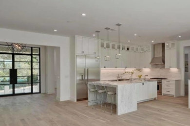 Inspiration for a mid-sized transitional l-shaped medium tone wood floor and brown floor eat-in kitchen remodel in Other with a farmhouse sink, shaker cabinets, white cabinets, marble countertops, gray backsplash, stainless steel appliances, an island and gray countertops