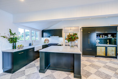Modern open plan kitchen in Brisbane with a farmhouse sink, shaker cabinets, green cabinets, solid surface benchtops, white splashback, ceramic splashback, black appliances, porcelain floors, with island, white benchtop and timber.